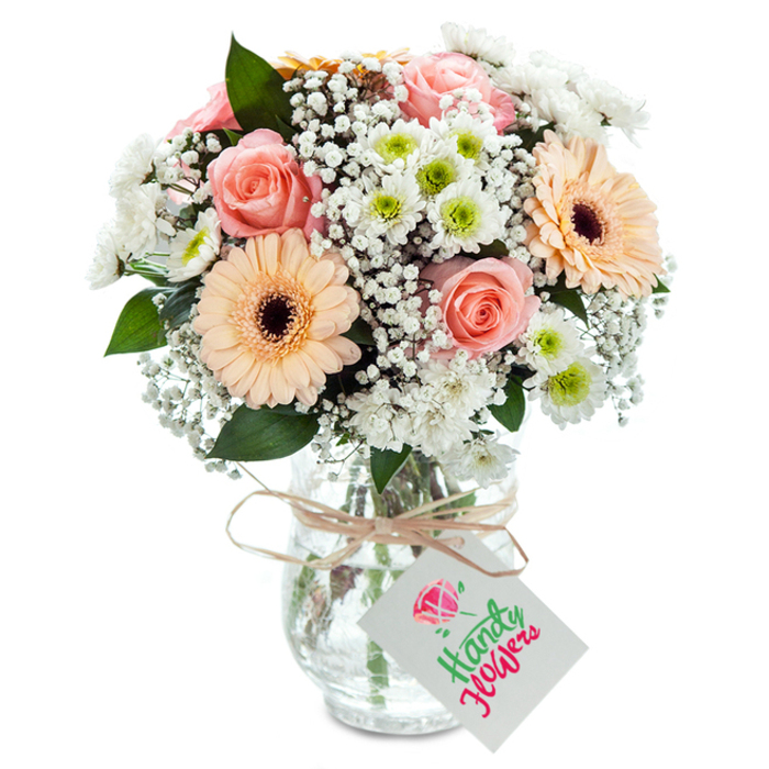 Arranged with care, this fresh floral bouquet epitomizes the storied charm of Uxbridge living. At its heart lie sumptuous peach-pink roses, sultry and inviting, surrounded by cheerful peach gerbera daisies whose broad petals and deep brown centers add a lively spirit. Airy baby's breath softens each angle, creating a gentle, cloud-like diffusion of white that brightens the pastel palette. Dotted amongst them are crisp white chrysanthemums, their lively green centers lending a sense of growth and newness that calls to mind strolls along Rockingham Road. Sinuous green foliage outlines each bloom, its subtle herbal notes reinforcing the bouquet's connection to the riverside air just beyond the city center. All are placed in a classic clear glass vase, subtle in its textured finish yet elegant in presence-the stems inside celebrating both the bounty of the arrangement and the purity of the water. Around the neck, natural twine is tied in a carefully considered bow, a blank tag hanging from it, waiting for a thoughtful note penned by a resident of Uxbridge. The bouquet's gentle blend of hues and textures is ideal for expressing gratitude, elevating a simple dinner table, or honoring a loved one with an unexpected weekday delivery from the local florist.